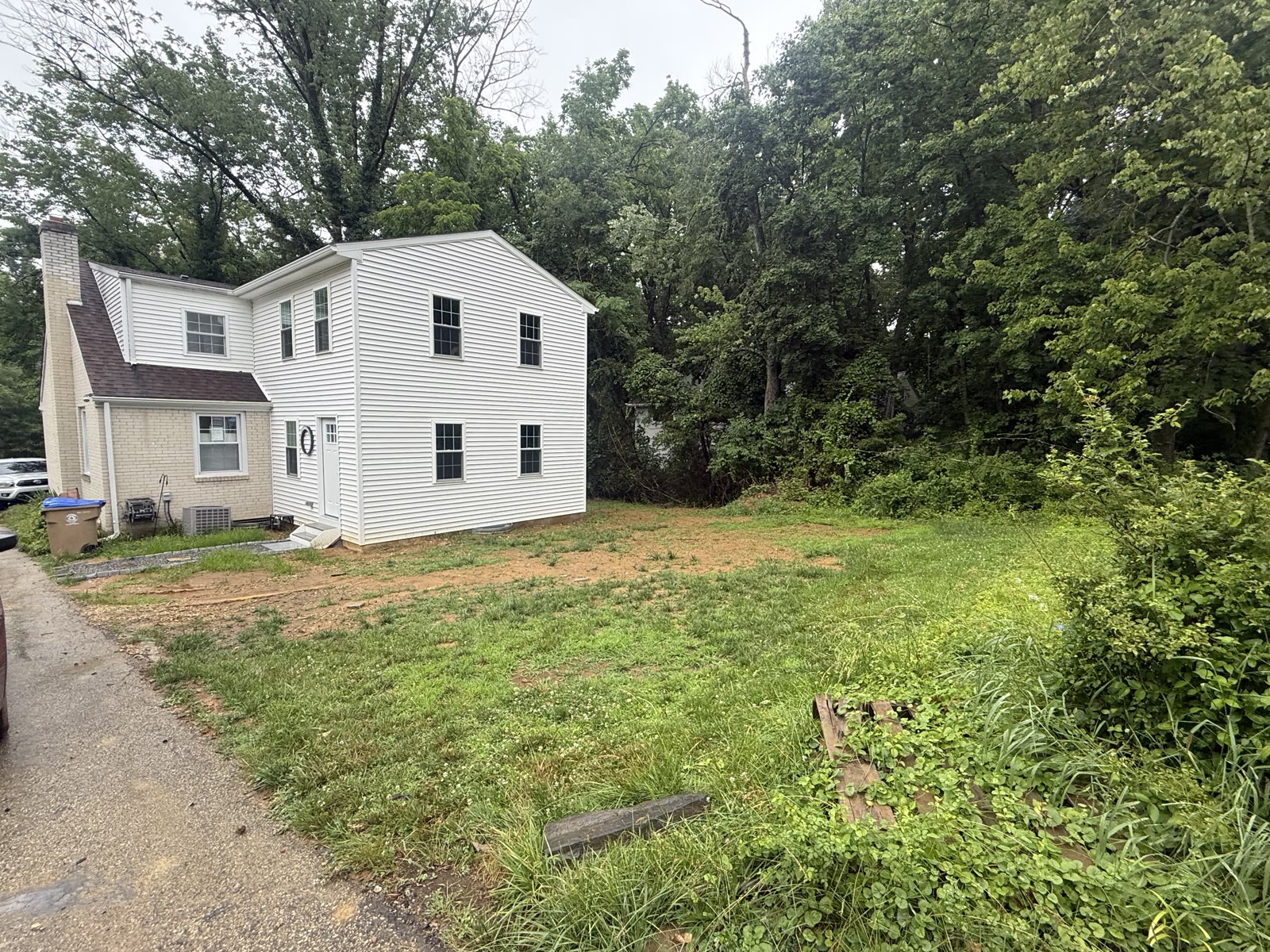 Overgrown, poorly graded yard beside the house before drainage work, where rainwater pooled against the foundation