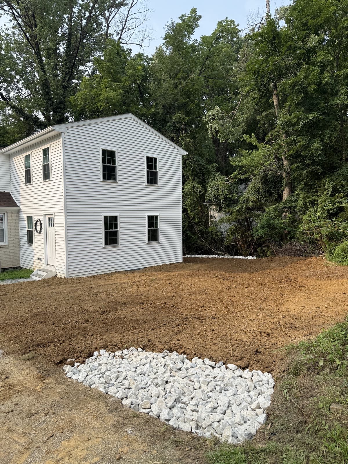Overgrown, poorly graded yard beside the house before drainage work, where rainwater pooled against the foundation
