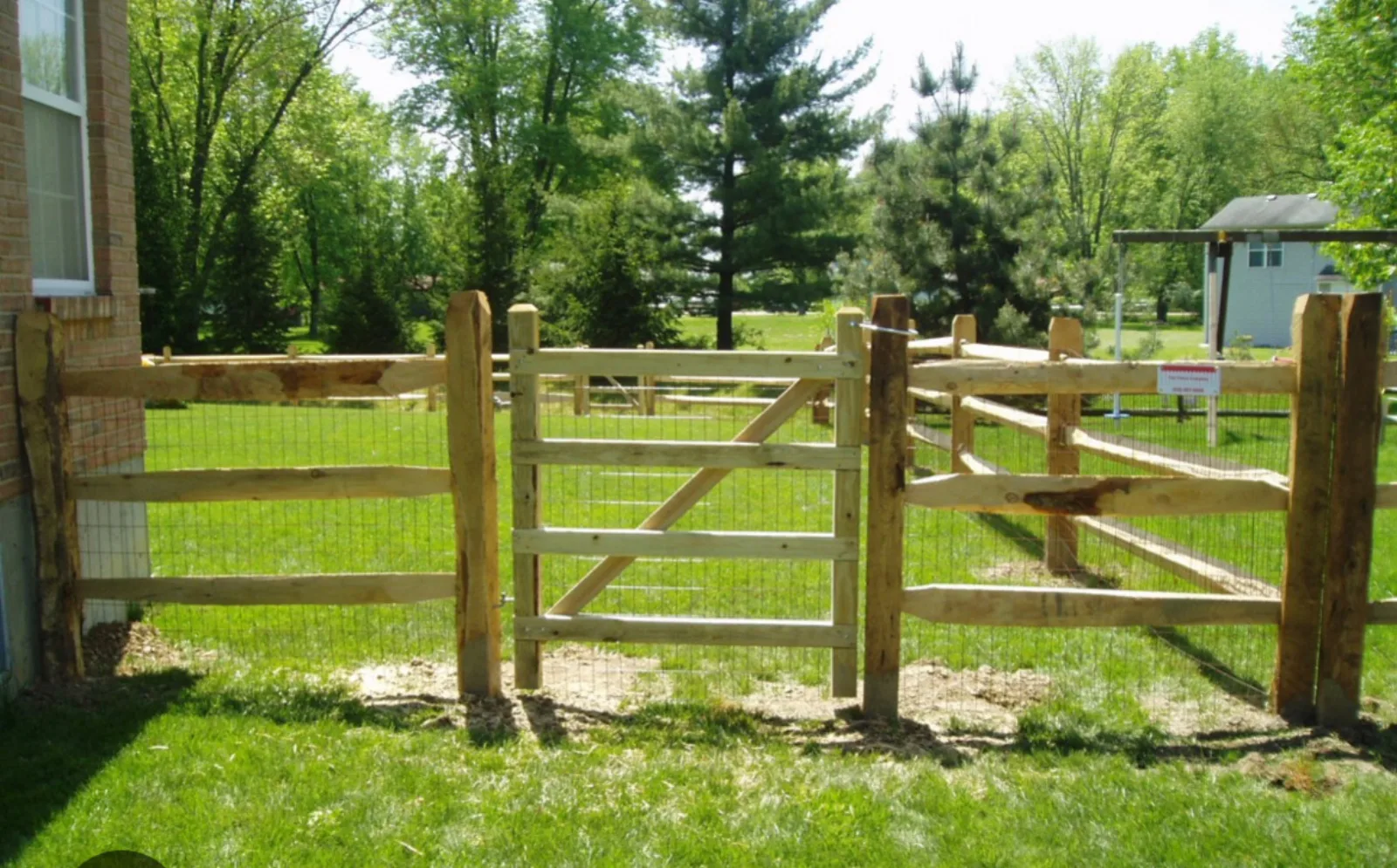 Split rail fence with a wood gate and welded wire backing beside a brick home