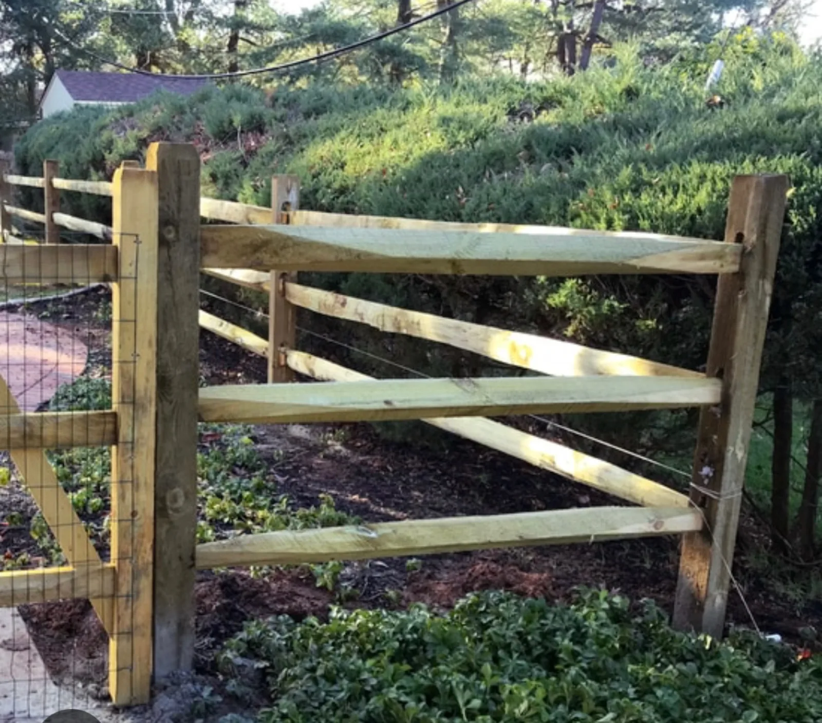 New split rail fence with welded wire mesh backing on a planted hillside