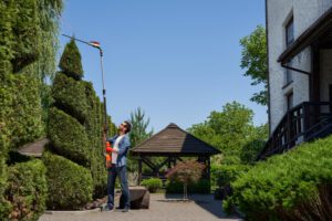 Landscaper using high altitude hedge trimmer